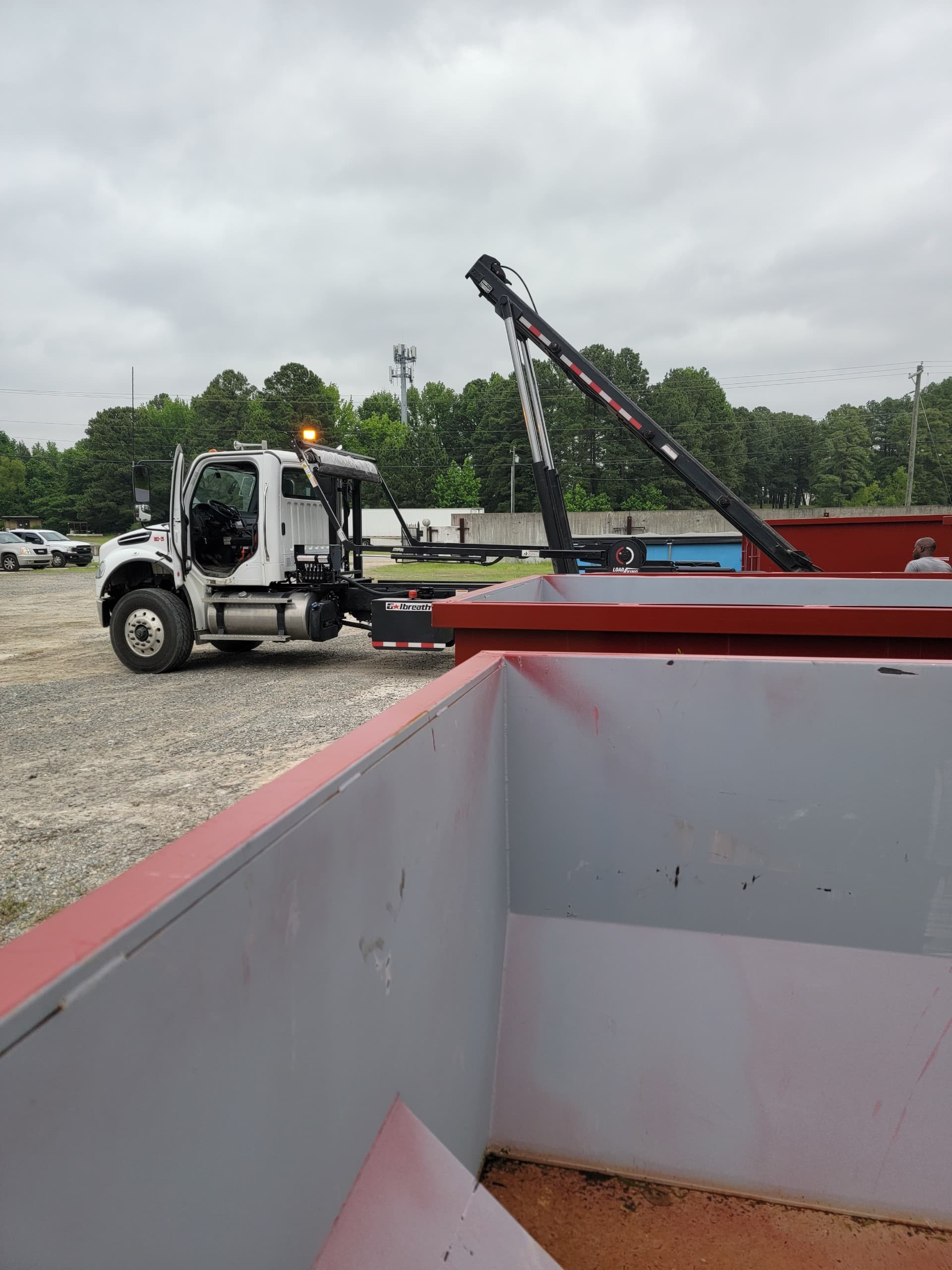 Truck near open red dumpster under cloudy sky
